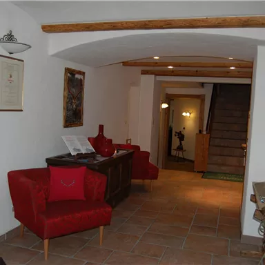 Ein einladender Empfangsbereich mit roten Sofas und warmem Licht. Im Hintergrund führt eine Treppe nach oben.