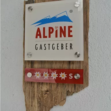 A sign with the inscription "ALPINE HOST" on a wooden background. Below it are stars that indicate a rating.
