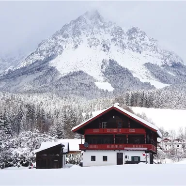 A picturesque mountain landscape with snow-capped peaks and a traditional chalet in the foreground. The winter magic creates a calm and idyllic atmosphere.