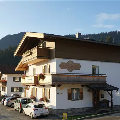 Ein charmantes Gebäude in den Alpen mit einem schönen Holzbalkon. Umgeben von grünen Wiesen und Bergen.