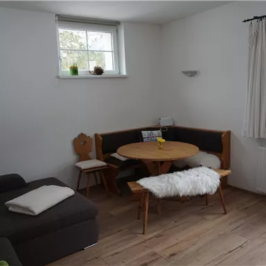 A cozy living space with a round dining table and seating area. The wooden floor and natural light create an inviting atmosphere.