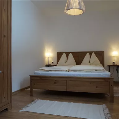 A cozy bedroom with a wooden bed and two pillows. Lamps hang on the walls, and the floor is covered with a carpet.
