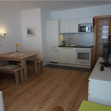 A modern living room with an open kitchen. There is a dining table, a couch, and a television.