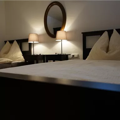 A cozy bedroom with two beds and warm light. The walls are in neutral colors, and a round mirror reflects the gentle lighting.