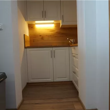A modern kitchen with white cabinets and wood details. The floor is made of wood and it is well lit.