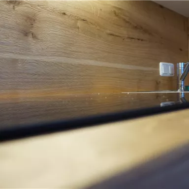 A modern wooden kitchen countertop with a glossy area. In the background, a faucet and an electrical outlet are visible.