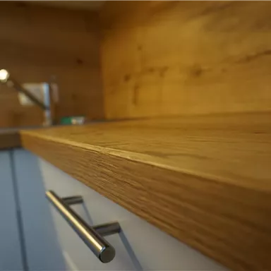 A modern kitchen with a beautiful wooden countertop and bright cabinets. The wall is made of wood and creates a cozy atmosphere.