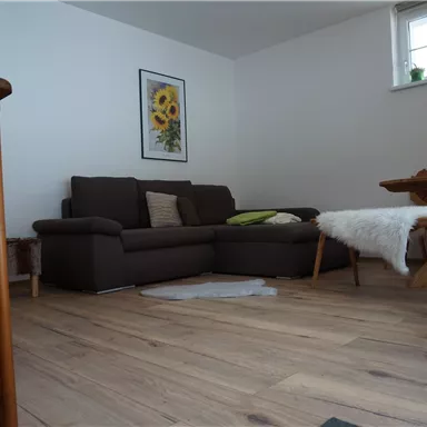 A cozy living space with a brown sofa and a wooden dining table. A painted picture of sunflowers hangs on the wall.