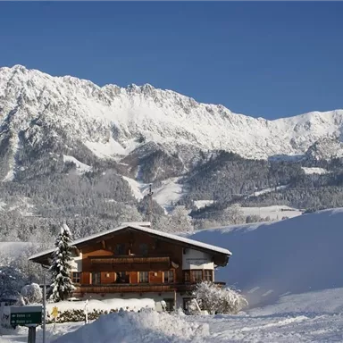 A charming wooden house in a snowy winter landscape. In the background, majestic mountains rise under a clear blue sky.
