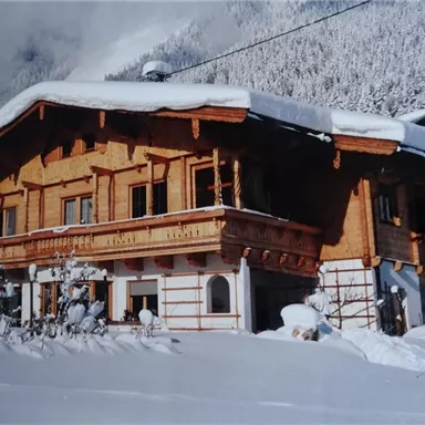 Ein charmantes Holzhaus im Schnee, umgeben von winterlicher Landschaft. Die Fassade ist traditionell gestaltet und die Umgebung ist friedlich und schneebedeckt.
