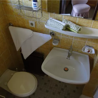 A small bathroom with a toilet and a sink. Towels hang on the wall and toiletries are placed on a shelf.