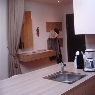 Eine moderne Küche mit einer Holzarbeitsplatte und einem Waschbecken. Im Hintergrund sind eine Gardine und einige Küchenutensilien zu sehen.