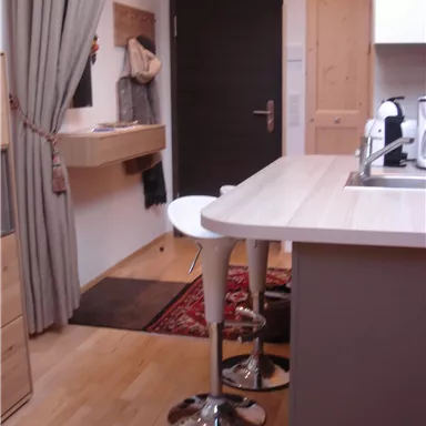 Eine moderne Küche mit einem Bartisch und Hockern. Der Raum ist hell und einladend, mit Holz- und Stoffelementen.