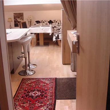 Ein gemütlicher Raum mit modernem Mobiliar und hellem Holzboden. Der Blick geht durch die Tür auf einen Tisch und eine stilvolle Sitzgelegenheit.