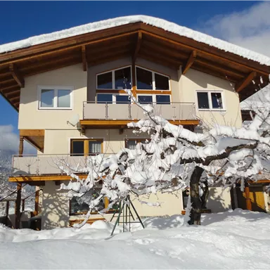 A cozy house in the snow with a beautiful wooden roof. The surroundings are wintry with snow-covered trees.