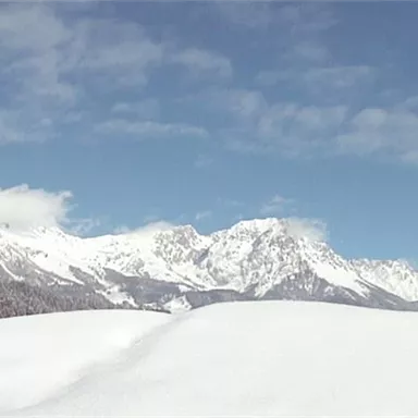 A winter landscape with snow-covered mountains and a clear sky. The view shows a calm, frozen environment.