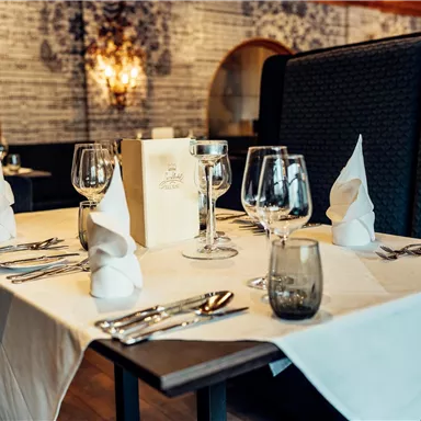 An elegantly set table in a restaurant. The tablecloth is white and the glasses and cutlery are neatly arranged.