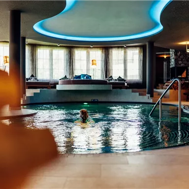 An elegant pool area with soft lights and a relaxing ambiance. One person is swimming in the water and enjoying the calm atmosphere.