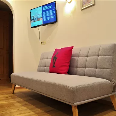 A modern living room with a gray sofa and a red cushion. A television is mounted on the wall, displaying information.