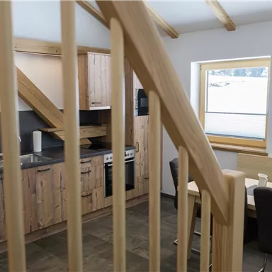 Eine moderne Küche mit Holzschränken und modernen Geräten. Der Raum hat große Fenster, die viel Tageslicht hereinlassen.