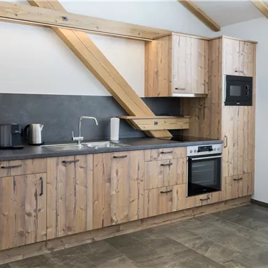 Eine moderne Küche aus Holz mit stilvollen Schränken und einer dunklen Arbeitsfläche. Die Ausstattung umfasst einen Kühlschrank, einen Ofen und eine Spüle.
