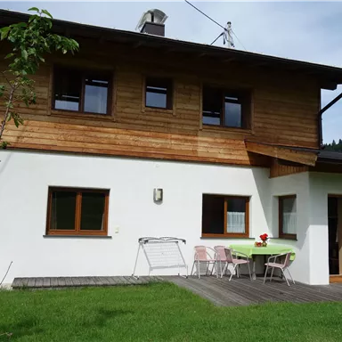A lovely house with wooden cladding and a white facade. In the foreground, there is a terrace with a table and chairs.