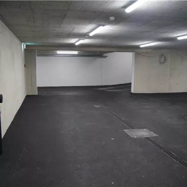 An empty parking lot in a building, with gray-painted walls and a smooth asphalt surface. The lighting is bright and even.