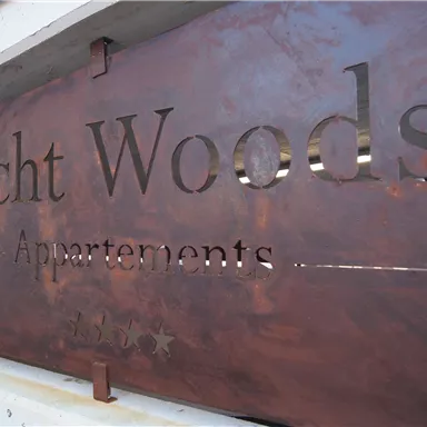 A sign made of rusty metal with the inscription "Echt Woods Apartments". It is mounted on the wall and shows the name of a residential complex.
