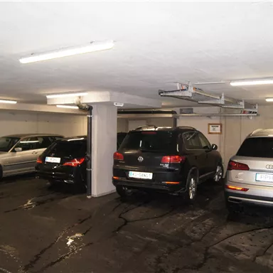 A parking garage with several vehicles. A gray BMW, a black SUV, and a silver Audi are visible.