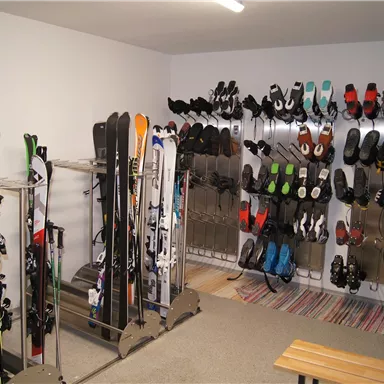 A ski room with numerous skis and snowboards. Many ski boots in different colors are hanging on the walls.
