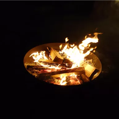 A warming campfire in a fire pit. The flames dance over the wood and illuminate the darkness.