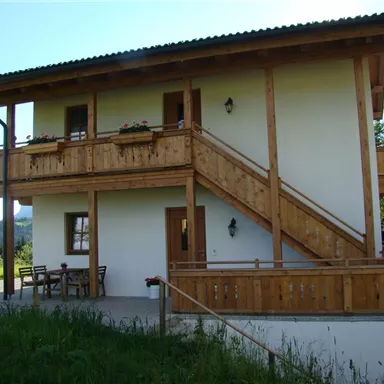 Ein schönes Holzhaus im Alpenstil mit einem Balkon und einer Treppe. Umgeben von grünen Wiesen und Bäumen.