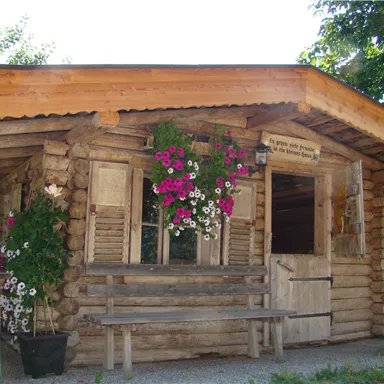 A rustic wooden house with a beautiful porch. Flowers hang in front of the window, giving the building an inviting atmosphere.
