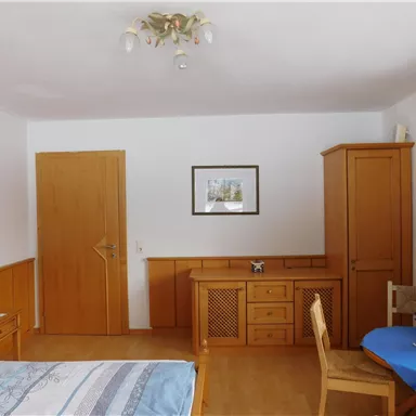 A cozy room with wooden furniture and a small table. On the wall hangs a picture, and the windows are decorated with blue curtains.