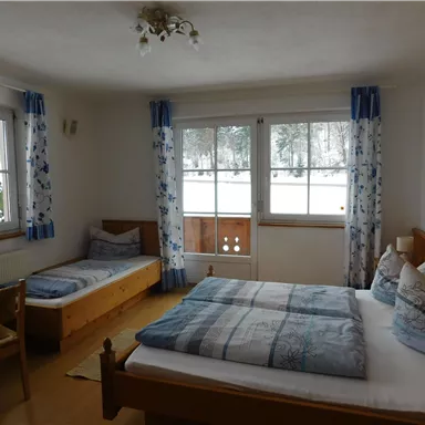 A cozy room with two beds and a large window. The walls are bright, and the curtains have a floral design.