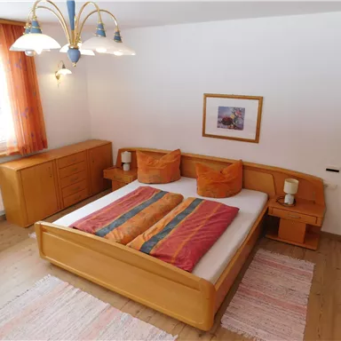 A cozy bedroom with a large bed and colorful pillows. The room is bright, designed with wood and fabric elements.