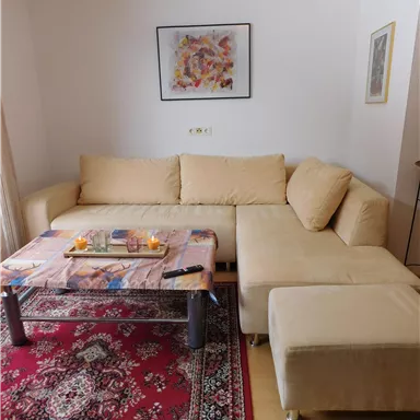 A cozy living room with a bright couch and a coffee table. Candles are placed on the table, and the walls are decorated with art pictures.