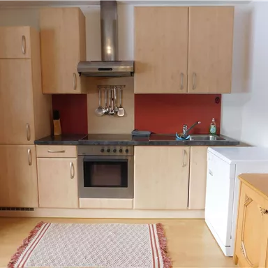 A modern kitchen with wooden cabinets and an integrated oven. The kitchen also includes a refrigerator and is well-equipped.