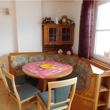 A cozy dining area with a U-shaped bench and a round table. A wooden cabinet with decorations stands against the wall.