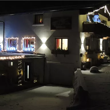 Ein charmantes Haus im Schnee mit festlicher Beleuchtung und einem Weihnachtsbaum. Es strahlt eine gemütliche Atmosphäre in der Winternacht aus.