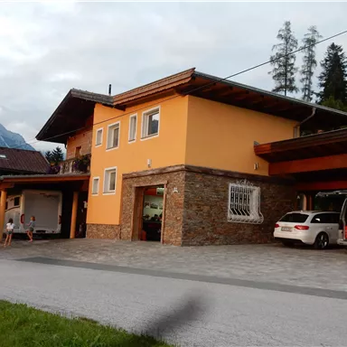 Ein modernes Haus mit einer orangefarbenen Fassade und Steinverkleidung. Im Vordergrund sind Autos auf der Einfahrt geparkt.