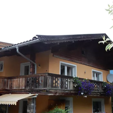 Ein gemütliches Haus mit einem Balkon und Blumenkästen. Die Fassade ist in warmen Farbtönen gehalten.