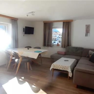 Ein heller Wohnraum mit einem gemütlichen Sofa und einem Tisch. Große Fenster sorgen für viel Tageslicht.