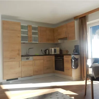 Eine moderne Küche mit Möbeln aus hellem Holz. Sie enthält verschiedene Geräte und einen Tisch mit Stühlen.