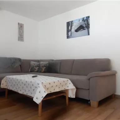 Eine gemütliche Wohnzimmereinrichtung mit einem großen Sofa und einem Tisch. An der Wand hängen Bilder, und es gibt einen Teppich auf dem Boden.