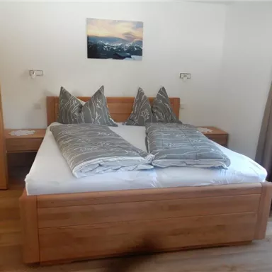 Ein gemütliches Schlafzimmer mit einem großen Doppelbett und stilvollen, grauen Kissen. An der Wand hängt ein Bild mit einer Berglandschaft.