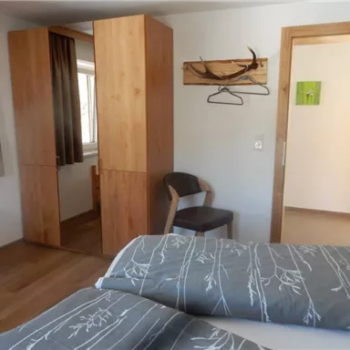 Ein gemütliches Schlafzimmer mit Holzmobiliar und zwei Betten. Die Wände sind hell, und es gibt einen kleinen Schreibtisch sowie einen Stuhl.