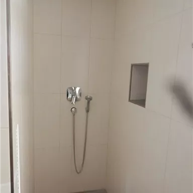 Eine moderne Dusche mit hellen Fliesen und einer Regendusche. Die Wand hat ein kleines Ablagefach.