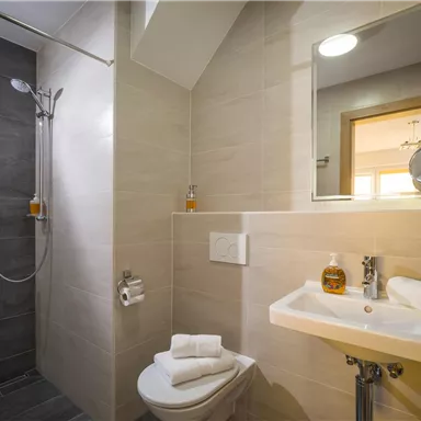 A modern bathroom with a shower and a sink. Towels and toiletries are neatly arranged on the sink.