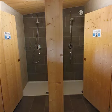 Zwei Duschkabinen mit Holzvertäfelung und modernen Duschköpfen. Die Wände sind gefliest und der Boden ist mit Fliesen ausgelegt.